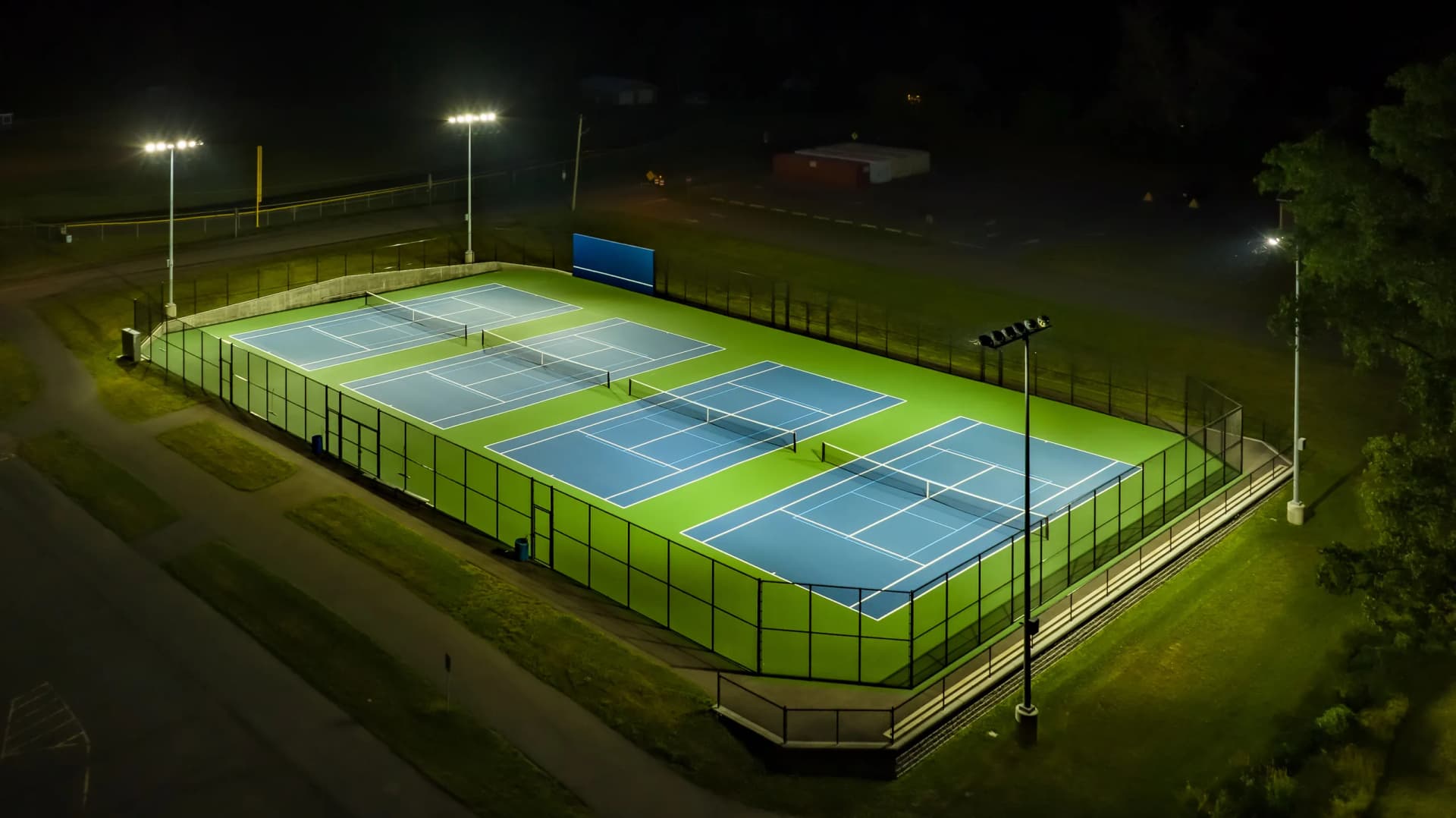 Aerial view of multiple illuminated tennis courts at night with bright floodlights.